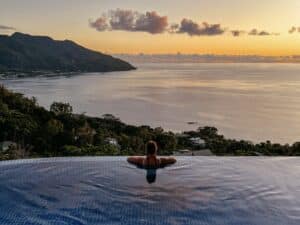 Reisende blickt vom Infinity Pool des Sorento Sur Mer Guesthouse auf Mahé, Seychellen, auf das Meer und den Sonnenuntergang
