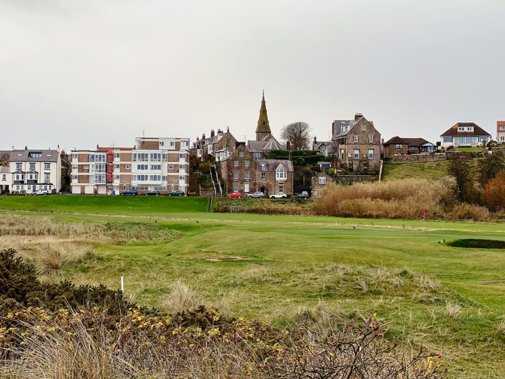 Blick vom Strand auf das Küstendorf Alnmouth mit Häusern, Kirche und Golfplatz
