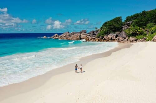 Drohnenaufnahme eines Paares beim Spaziergang an der Grand Anse auf La Digue, Seychellen, mit weißem Sandstrand und türkisfarbenem Meer