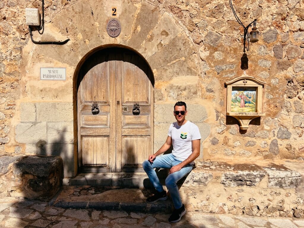 Lukas sitzt vor der Kirche Sant Joan Baptista in Deià auf Mallorca