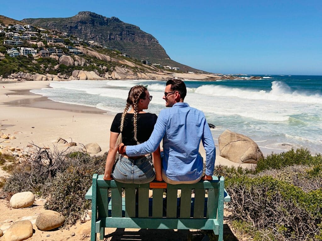 Franziska & Lukas von OurTravelWanderlust auf einer Bank am Llandudno Beach in Kapstadt in Südafrika, einem der schönsten Strände Kapstadts